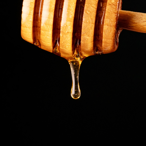 Wooden honey dipper with honey dripping against a black background